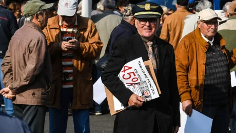 Bărbat cu pălărie și afiș, înconjurat de mulțime la un protest.