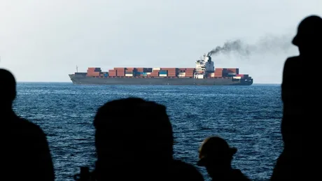 Vapor de marfă navigând pe mare, cu fum ieșind din chimenea.