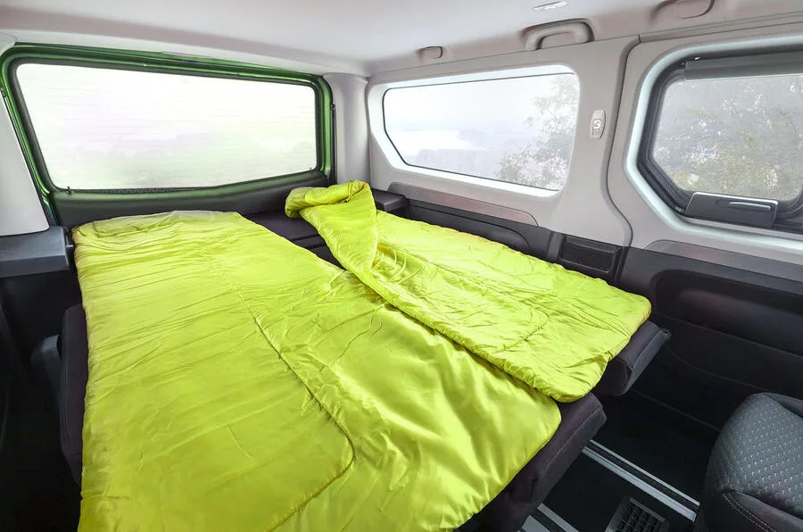 Interiorul unei autorulote imaginare, cu paturi verzi și feronerie simplă.