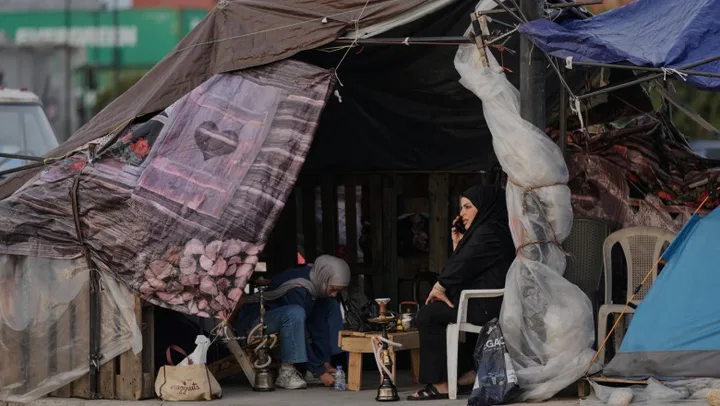 O femeie stă într-un cort improvizat, discutând la telefon, în mijlocul unei tabere.