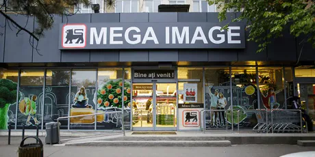 Magazin Mega Image cu produse variate și clienți la intrare.