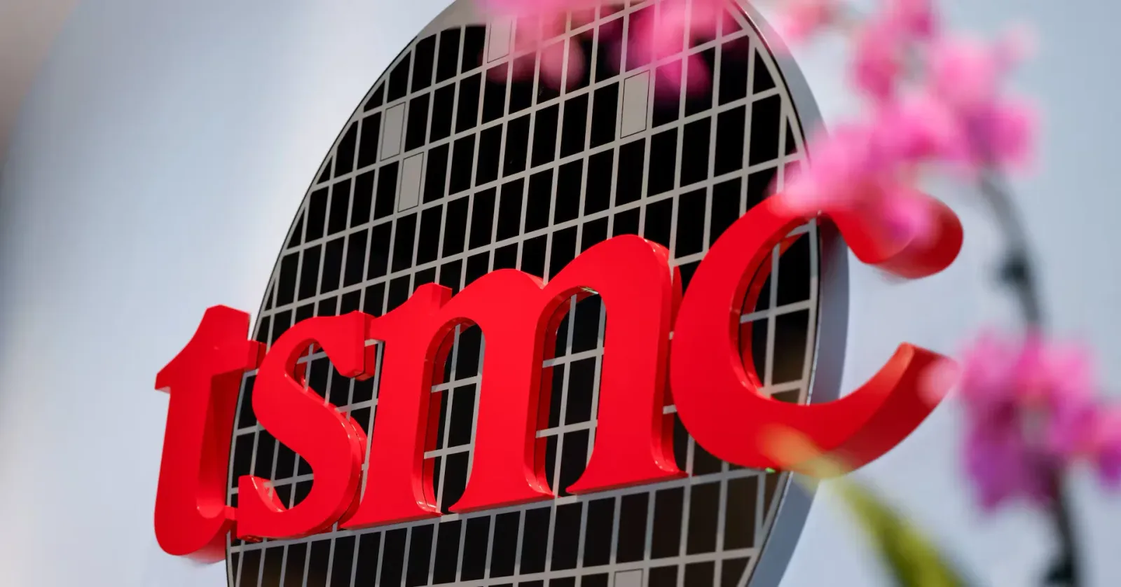 Logo-ul TSMC pe un fundal modern, cu flori în prim-plan.