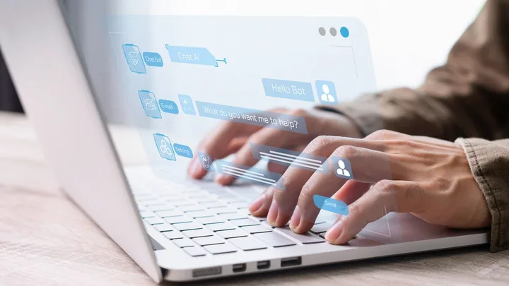 O persoană tastează pe un laptop, interacționând cu un chatbot.