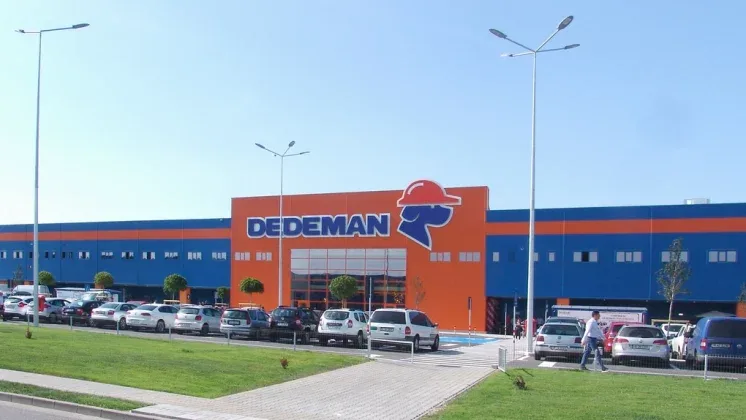Magazin Dedeman cu parcarea plină și cer senin.