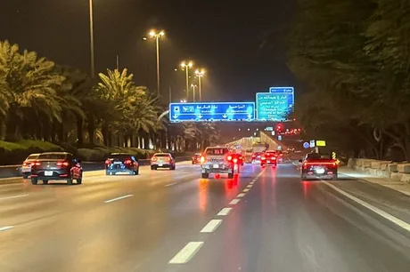 Stradă iluminată noaptea în Arabia Saudită, cu palmieri pe margine.