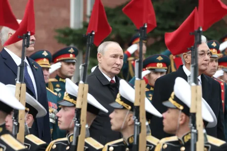 Ceremonie militară cu soldați și steaguri roșii în fundal.