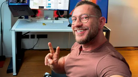 Peter Steinberger zâmbind în fața unui birou modern, cu laptop și ecrane.