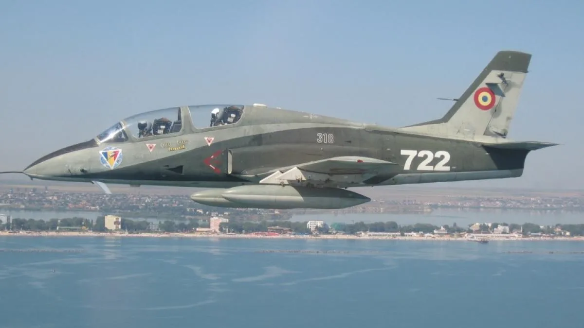 Avion IAR-99 Șoim zburând deasupra apei, simbol al industriei aeronautice românești.