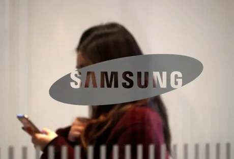 Logo Samsung pe un fundal alb, cu o persoană folosind telefonul mobil.