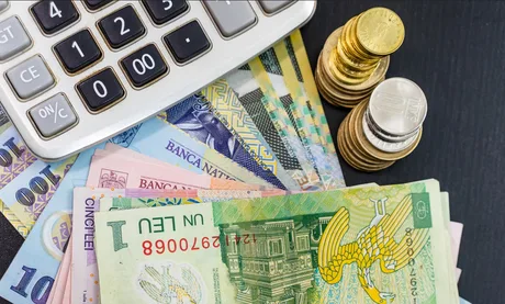 Bancnote și monede românești alături de un calculator.