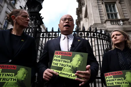 Activist pro-democrație discutând despre situația lui Jimmy Lai în fața unei clădiri guvernamentale.