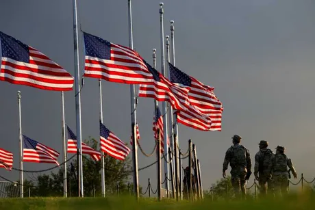 Militari americani merg pe un teren cu steaguri ale SUA în fundal.