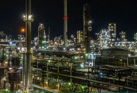 Rafinărie iluminată noaptea, cu instalații industriale complexe și lumini strălucitoare.