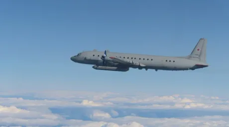 Avion militar zburând deasupra norilor în cerul albastru.