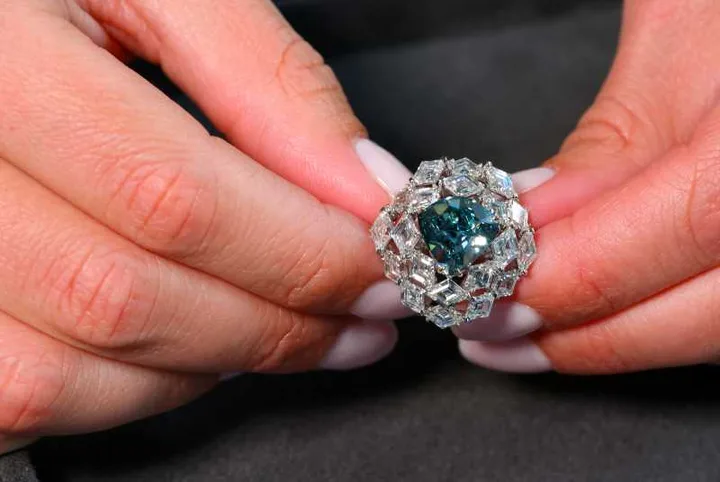 Un inel cu diamant albastru-verde strălucitor, în mâini.