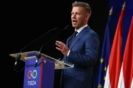 Un vorbitor la un eveniment, cu steaguri în fundal, discutând despre comunitate.