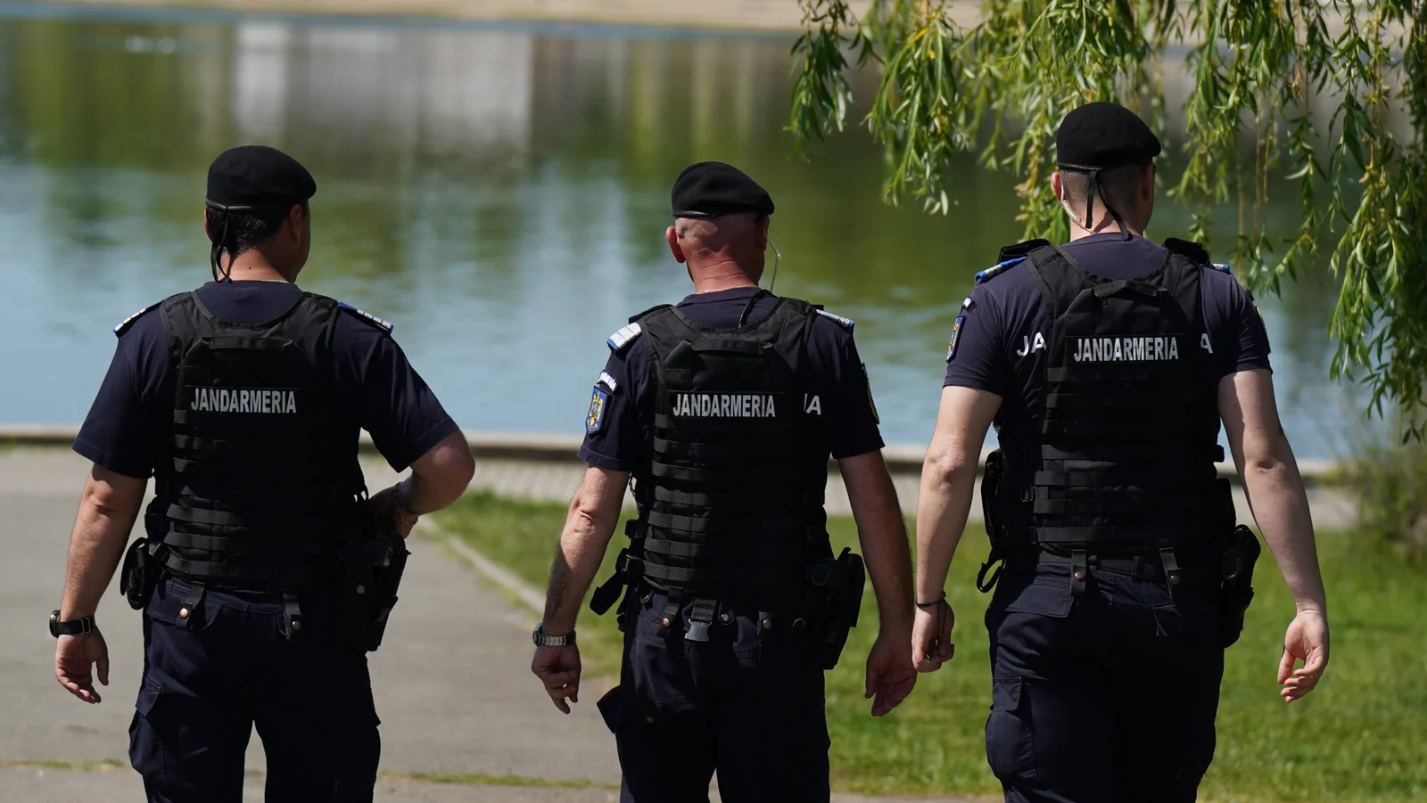 Trei ofițeri de poliție merg pe malul unui lac, purtând uniforme de serviciu.