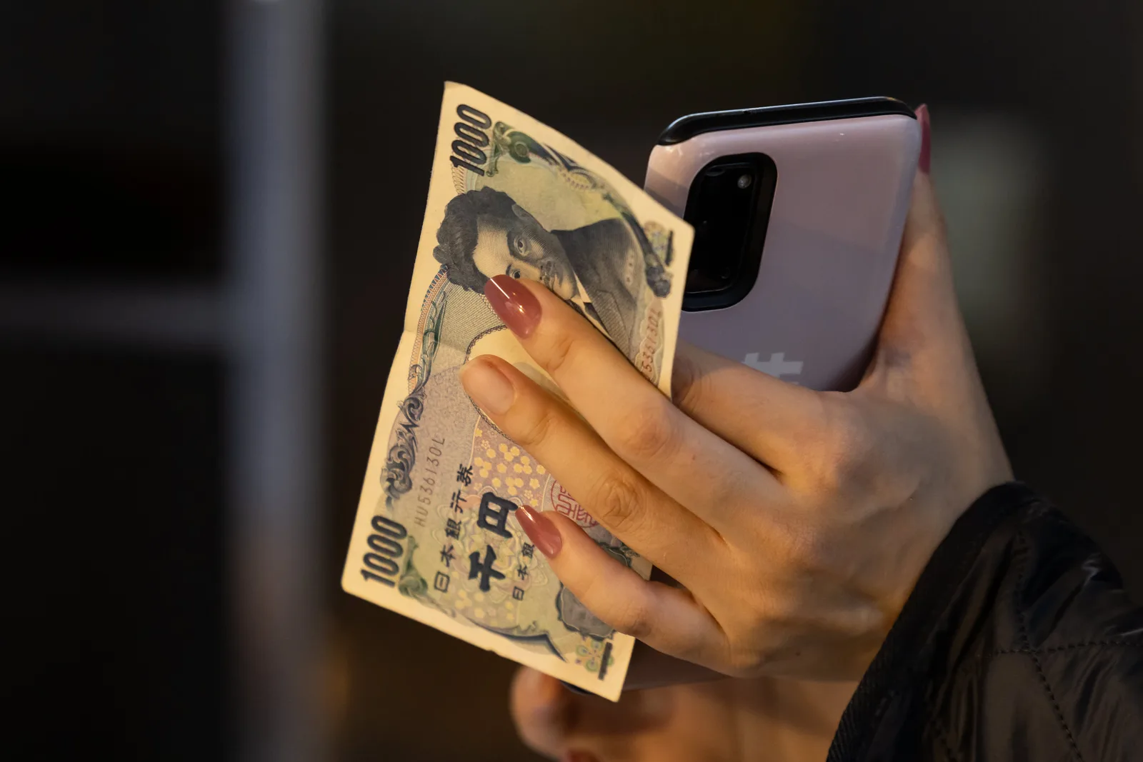 O persoană ține un telefon și o bancnotă de 1000 de yeni.