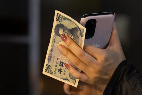 O persoană ține un telefon și o bancnotă de 1000 de yeni.