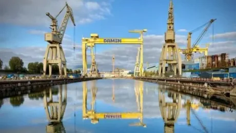 Șantierul Naval Damen Mangalia reflectat în apă, cu macarale mari în fundal.