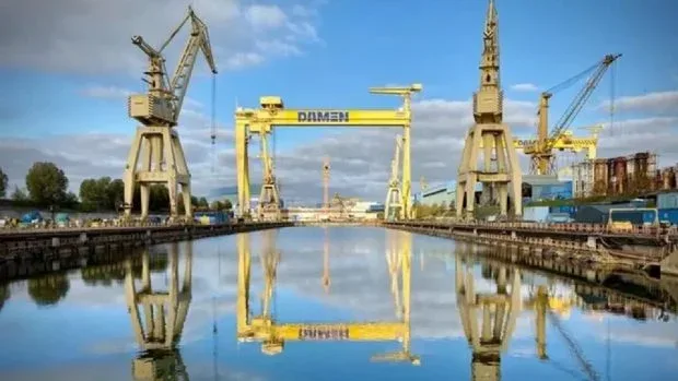 Șantierul Naval Damen Mangalia reflectat în apă, cu macarale mari în fundal.