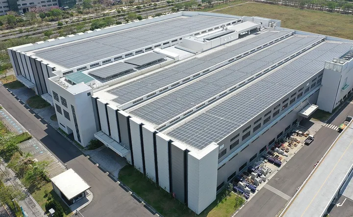 Clădire modernă cu panouri fotovoltaice pe acoperiș, înconjurată de natură.