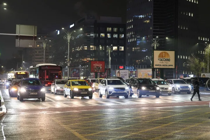 Intersecție aglomerată din București, cu vehicule și semafoare în fundal.