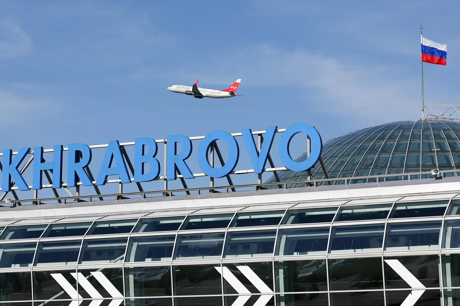 Aeroportul Khrabrovo din Kaliningrad, cu un avion în zbor și steagul Rusiei.