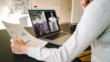 Persoană participând la o videoconferință pe laptop, analizând grafice și date.
