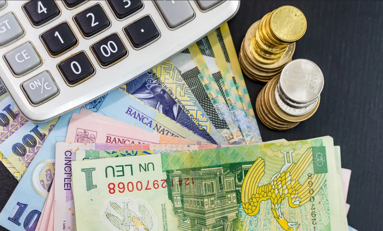Bancnote și monede românești alături de un calculator.