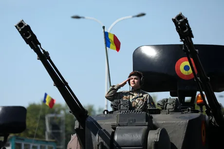 Soldat român pe un vehicul militar, salutând cu mândrie.
