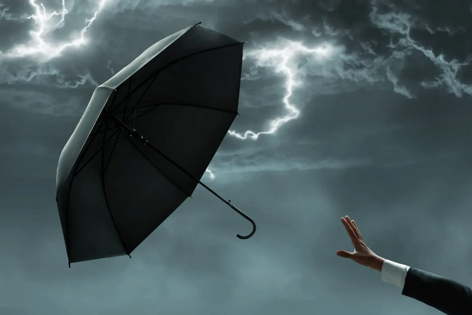 Umbrelă neagră în fața unui cer furtunos cu fulgere.