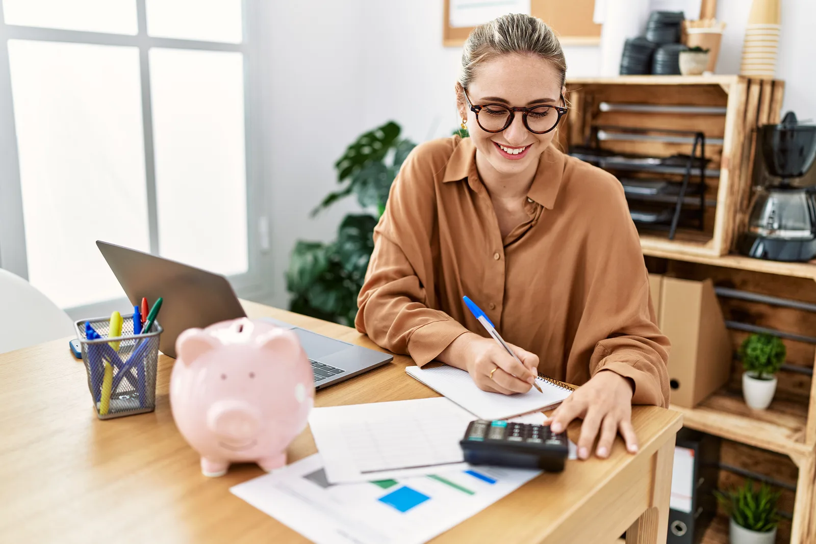 Femeie care lucrează la birou, notând informații financiare.