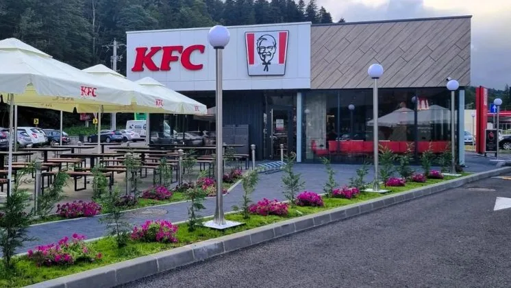 Restaurant KFC cu terasă și flori în față, într-o zonă verde.