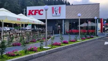 Restaurant KFC cu terasă și flori în față, într-o zonă verde.