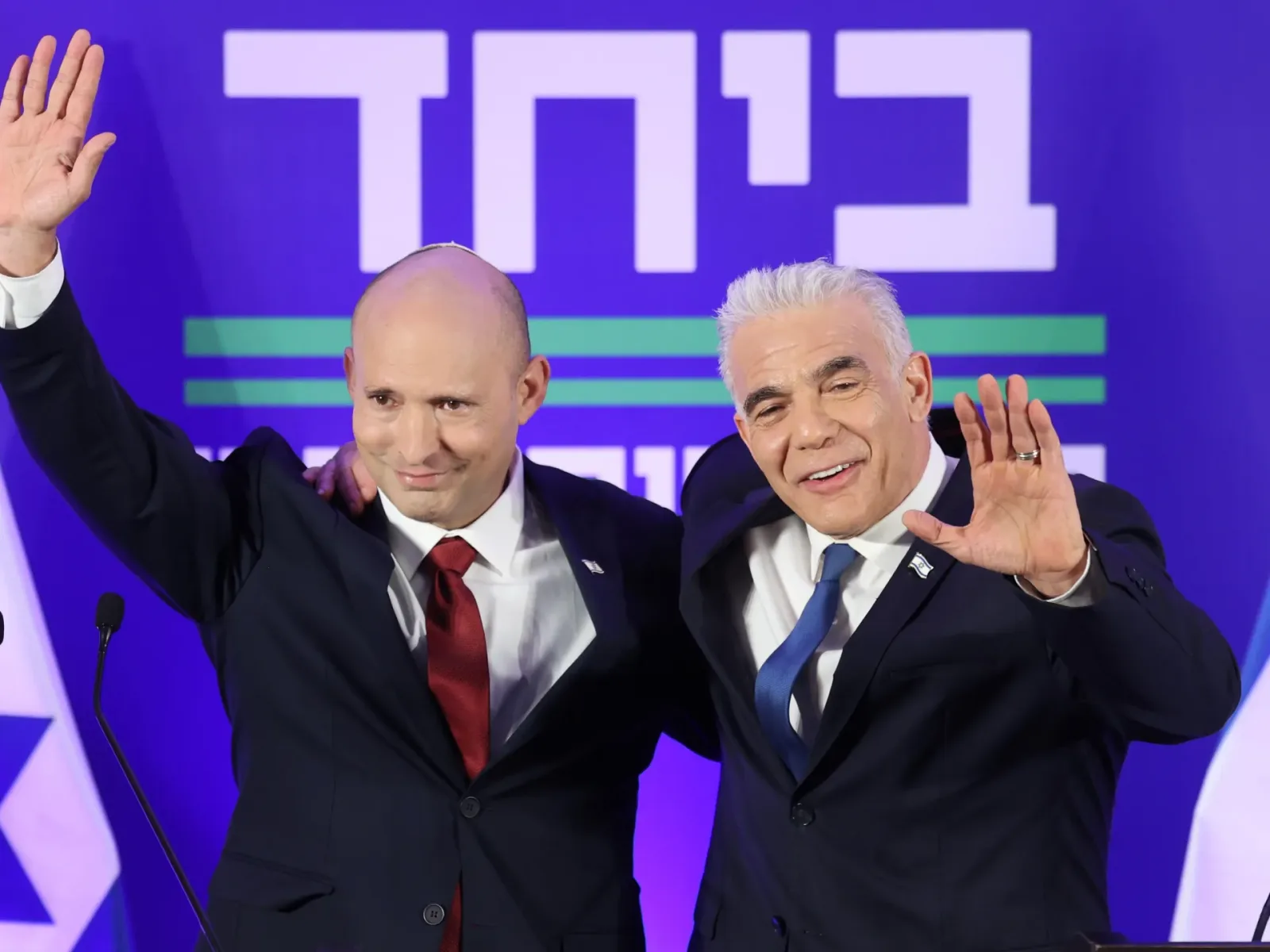 Naftali Bennett și Yair Lapid salută susținătorii în cadrul unei conferințe de presă.