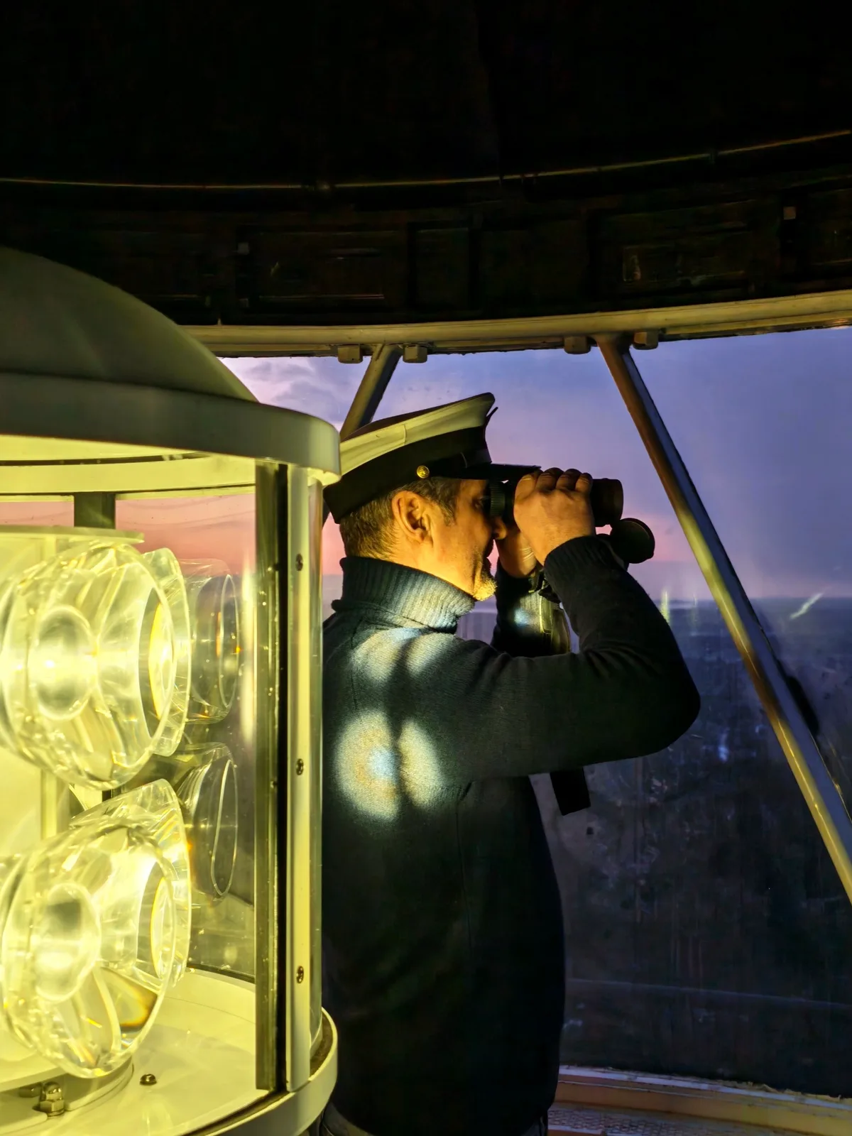 Un fotograf observând peisajul dintr-un far la apus.