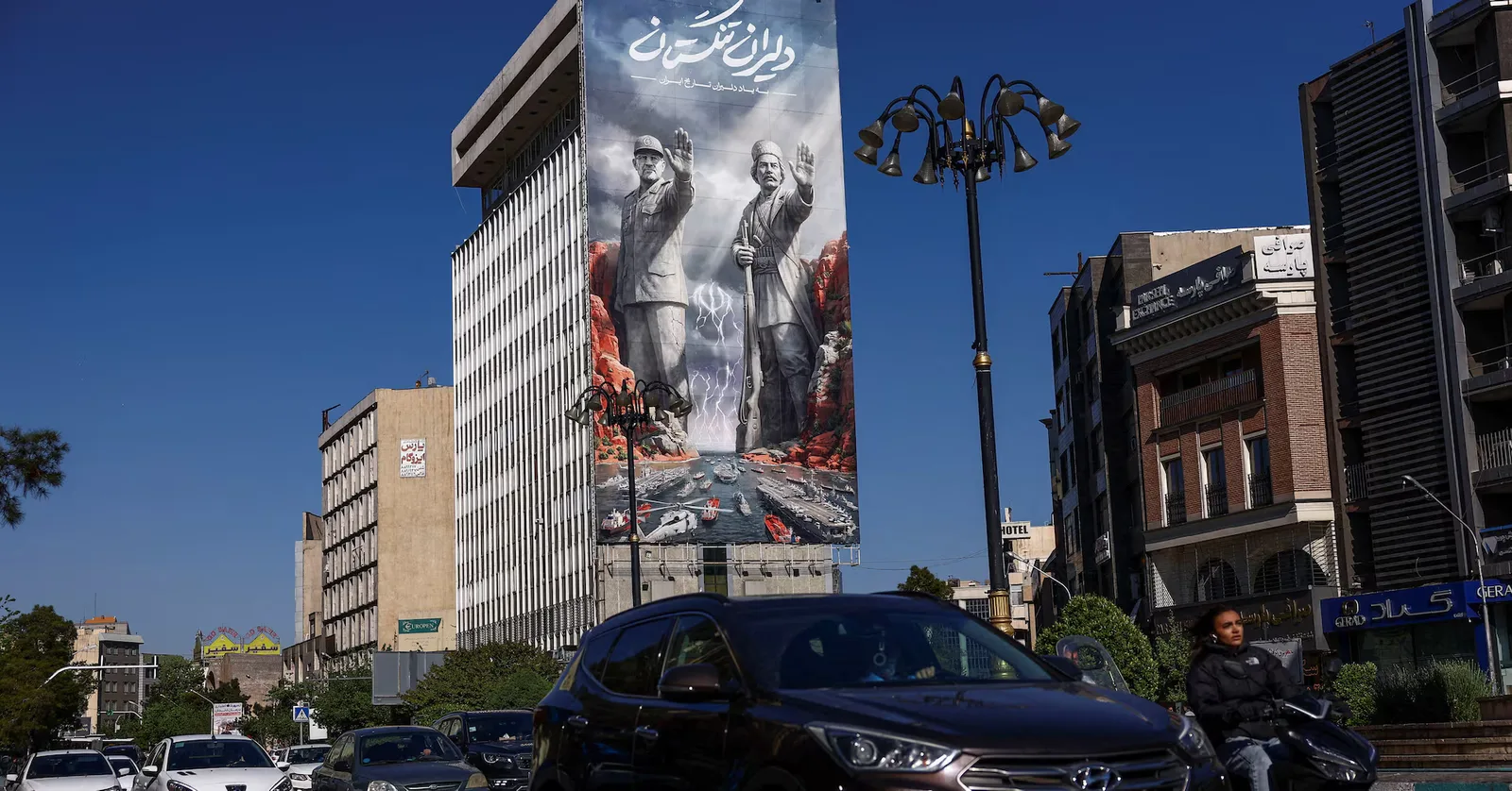 Un peisaj urban din Iran, cu clădiri și un banner mare pe fațada unei clădiri.