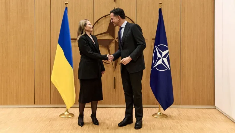 Întâlnire oficială între reprezentanți NATO și Ucraina, cu steaguri în fundal.