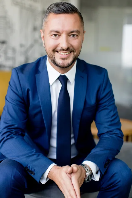 Alexandru Cristescu, reprezentant Raiffeisen, zâmbind în costum elegant.