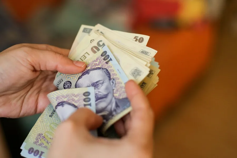 Bancnote românești în mâinile unei persoane, simbolizând veniturile și sporurile salariale.