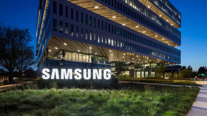 Sediul Samsung Electronics iluminat noaptea, cu vegetație în prim-plan.