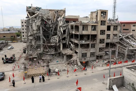 Clădiri distruse în urma conflictului, cu steaguri roșii și oameni în jur.