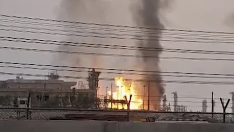 Flăcări și fum se ridică deasupra unei instalații industriale afectate.