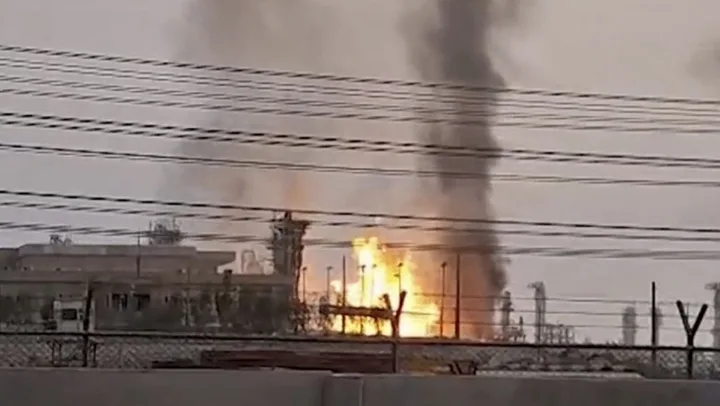 Flăcări și fum se ridică deasupra unei instalații industriale afectate.
