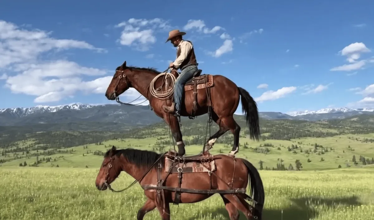 Cavaler pe un cal, echilibrându-se pe alt cal în peisaj montan.