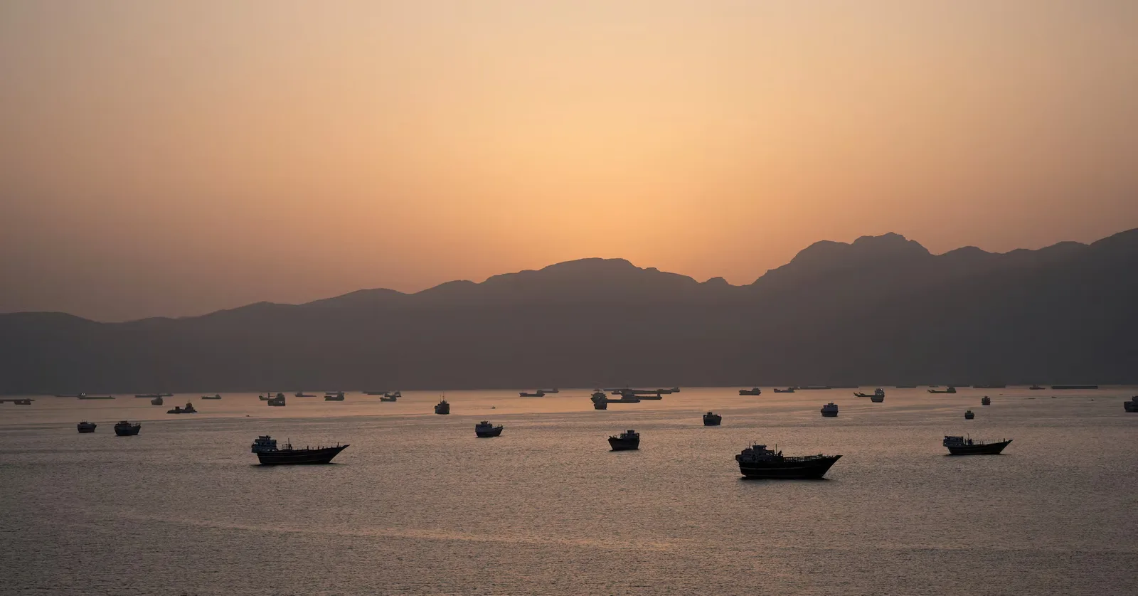 Vaporase ancorate în strâmtoarea Hormuz la apus, simbolizând tensiuni geopolitice.