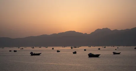 Vaporase ancorate în strâmtoarea Hormuz la apus, simbolizând tensiuni geopolitice.