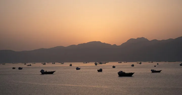 Vaporase ancorate în strâmtoarea Hormuz la apus, simbolizând tensiuni geopolitice.