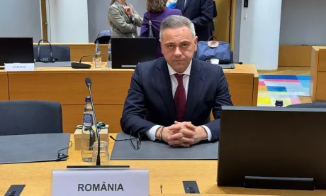 Un bărbat îmbrăcat elegant stă la o masă într-o sală de conferințe.